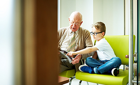 Indoors shot of little boy with his grandfather sitting in waiting room at dental clinic