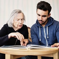 Young male volunteer reads a book with an elderly woman.