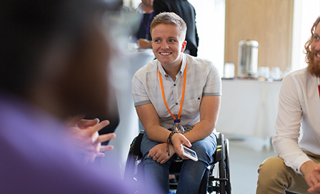 Smiling woman in wheelchair talking to colleagues in conference